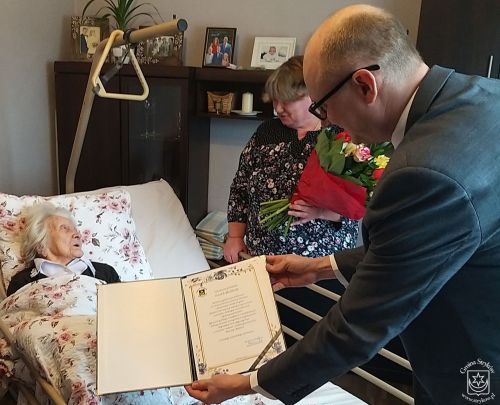 Jubilatka Pani Zofia Siuda w otoczeniu bliskich przyjmuje list gratulacyjny od Burmistrza Strykowa Witolda Kosmowskiego.